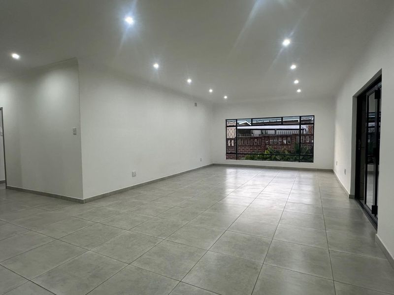 A spacious, bright, and empty living area featuring modern tiled flooring, recessed downlights, and large aluminium-framed windows and doors.