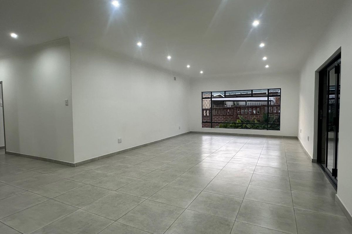 A spacious, bright, and empty living area featuring modern tiled flooring, recessed downlights, and large aluminium-framed windows and doors.