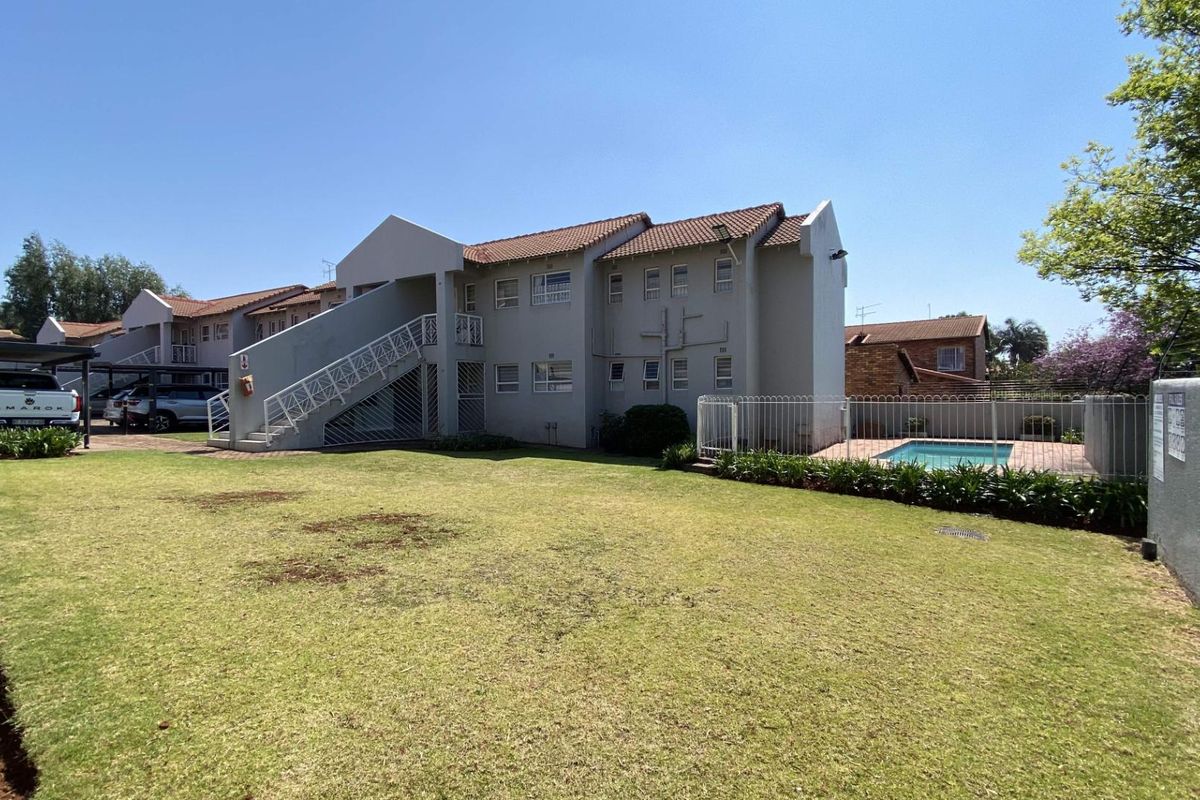 Rear view of the apartment complex featuring a communal swimming pool, landscaped lawn, and covered parking area.