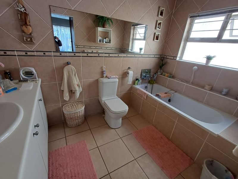 A functional bathroom featuring a built-in bathtub, vanity unit, and neutral ceramic tiling throughout, offering a clean and practical layout.
