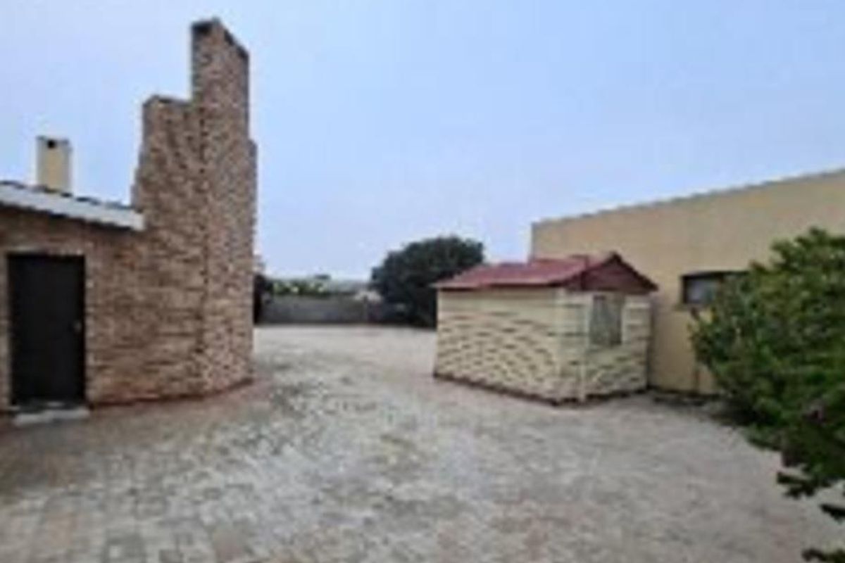 A rear courtyard area featuring paved ground, a prominent brick chimney structure, and a small detached storage shed.