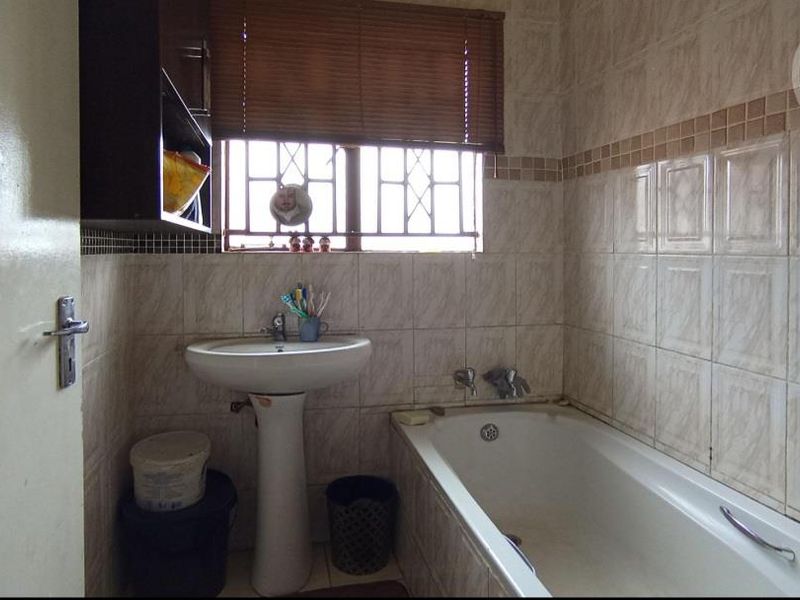 A functional bathroom featuring a pedestal basin, a built-in bathtub, and tiled wall finishes, requiring cosmetic updates to modernize the space.