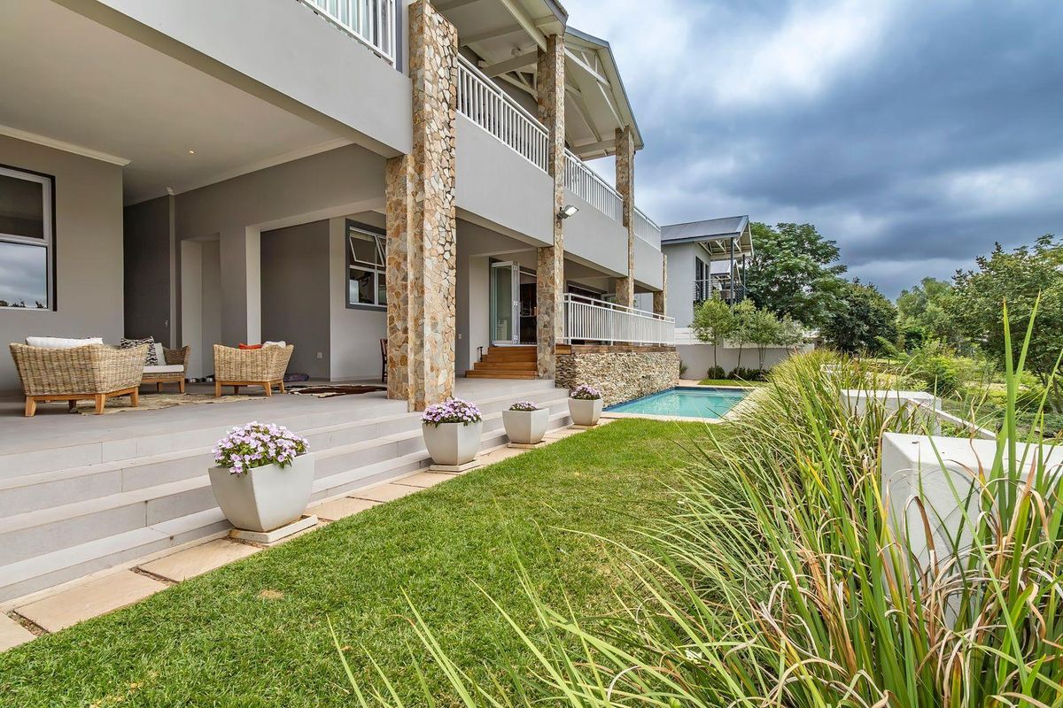 A spacious rear patio area featuring stone-clad pillars, tiled flooring, and direct access to a swimming pool and landscaped garden.
