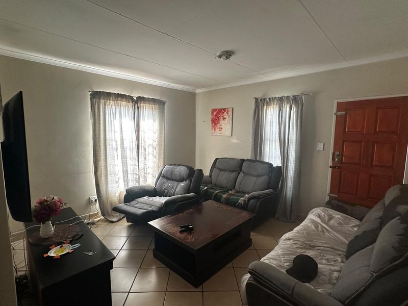 A functional living room featuring tiled flooring, coved ceilings, and a solid timber entrance door, providing a comfortable and practical living space.