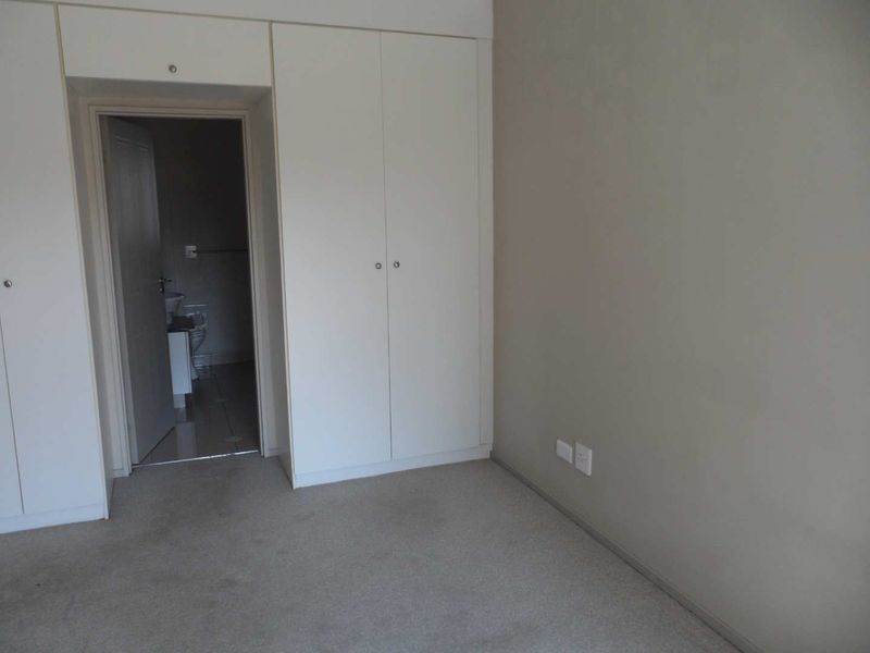 A neutral bedroom featuring built-in cupboards, carpeted flooring, and direct access to an en-suite bathroom.