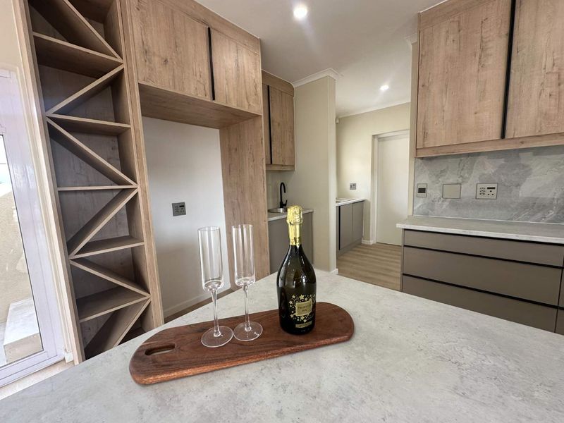 Modern kitchen featuring light wood-tone cabinetry, stone countertops, integrated wine storage, and a sleek backsplash, offering a clean and contemporary aesthetic.