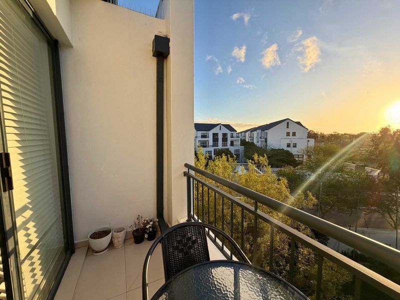 A private balcony featuring tiled flooring and a metal balustrade, offering pleasant sunset views over the surrounding neighborhood.