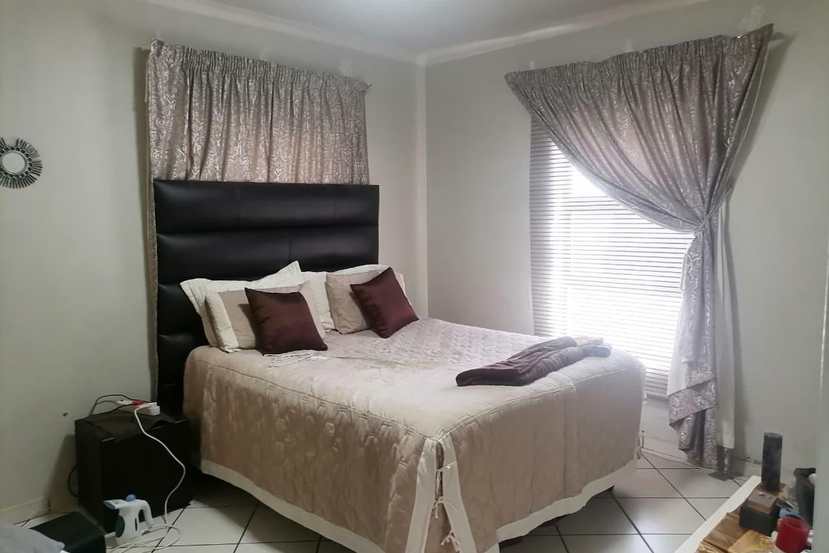 A bedroom featuring tiled flooring, neutral wall tones, and dual window treatments providing natural light.