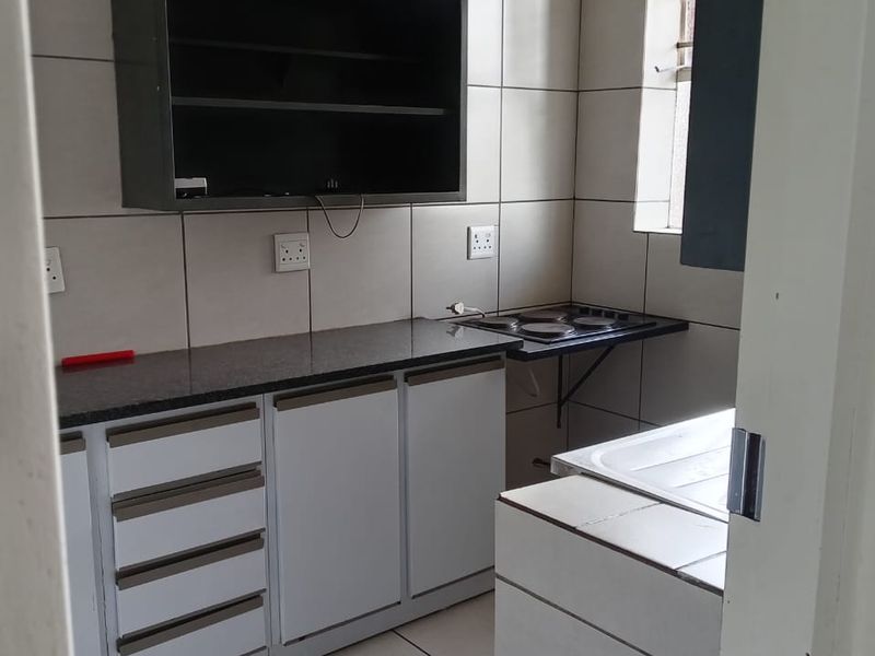 A compact kitchen featuring built-in cabinetry, granite countertops, an electric hob, and tiled finishes throughout.