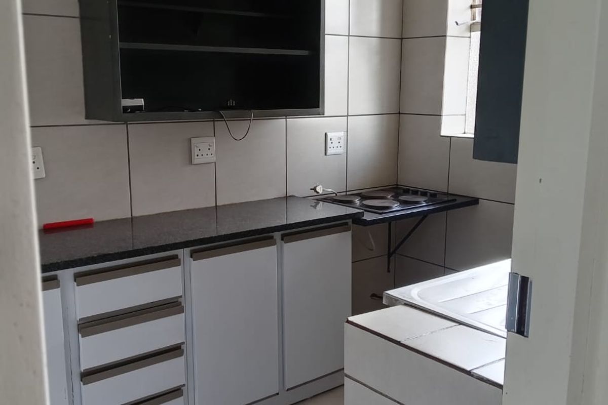 A compact kitchen featuring built-in cabinetry, granite countertops, an electric hob, and tiled finishes throughout.