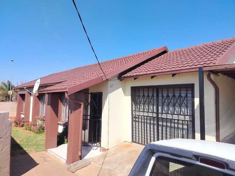 Front elevation of a single-story house featuring a tiled roof, security gates, and paved entrance area.