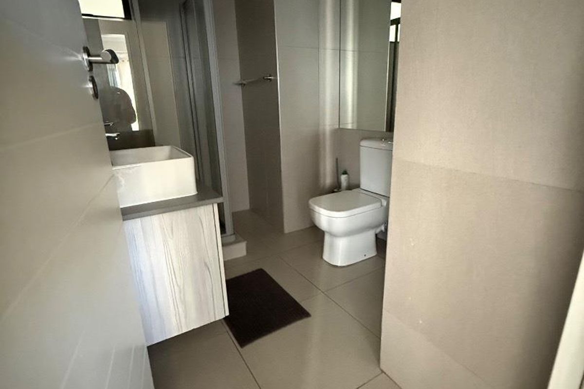 A modern bathroom featuring a vessel sink on a vanity cabinet, a toilet, and a glass-enclosed shower with neutral floor-to-ceiling tiling.
