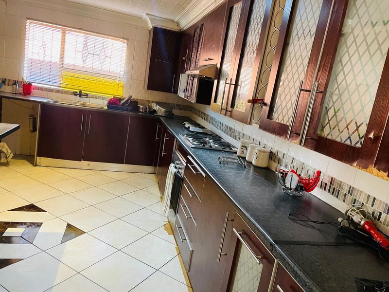 A functional kitchen featuring dark wood cabinetry, laminate countertops, a gas hob with extractor fan, and tiled flooring with a decorative inlay.