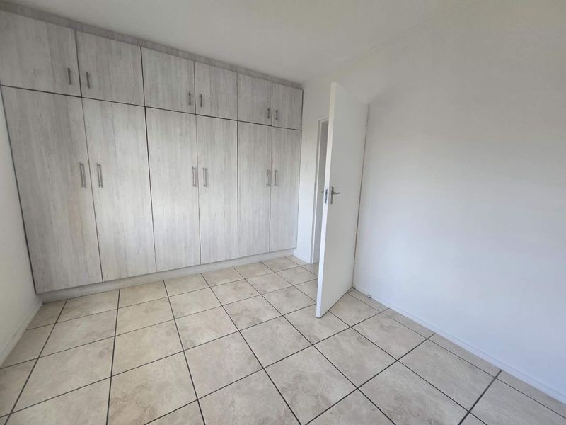 A clean, empty bedroom featuring light wood-grain built-in cupboards and neutral tiled flooring, offering a versatile space ready for personalization.