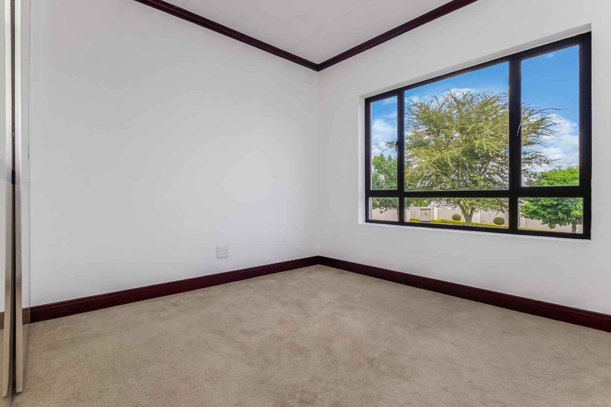 A bright, empty bedroom featuring neutral carpeting, dark trim detailing, and a large window providing natural light and exterior views.