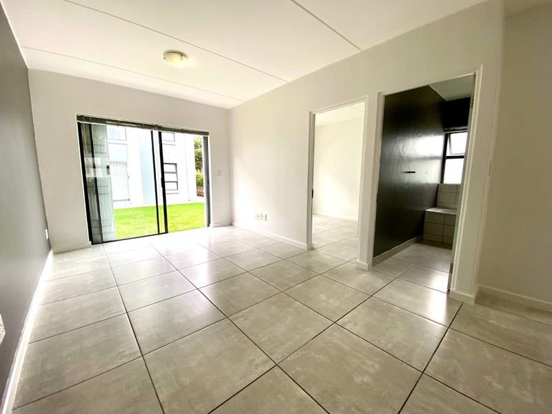 A bright, empty living area featuring large format floor tiles, neutral walls, and a sliding glass door providing access to the exterior.