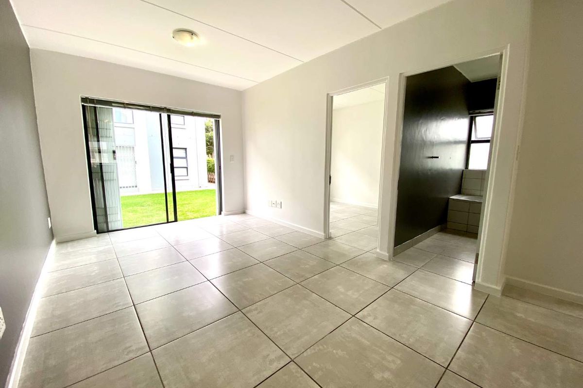 A bright, empty living area featuring large format floor tiles, neutral walls, and a sliding glass door providing access to the exterior.