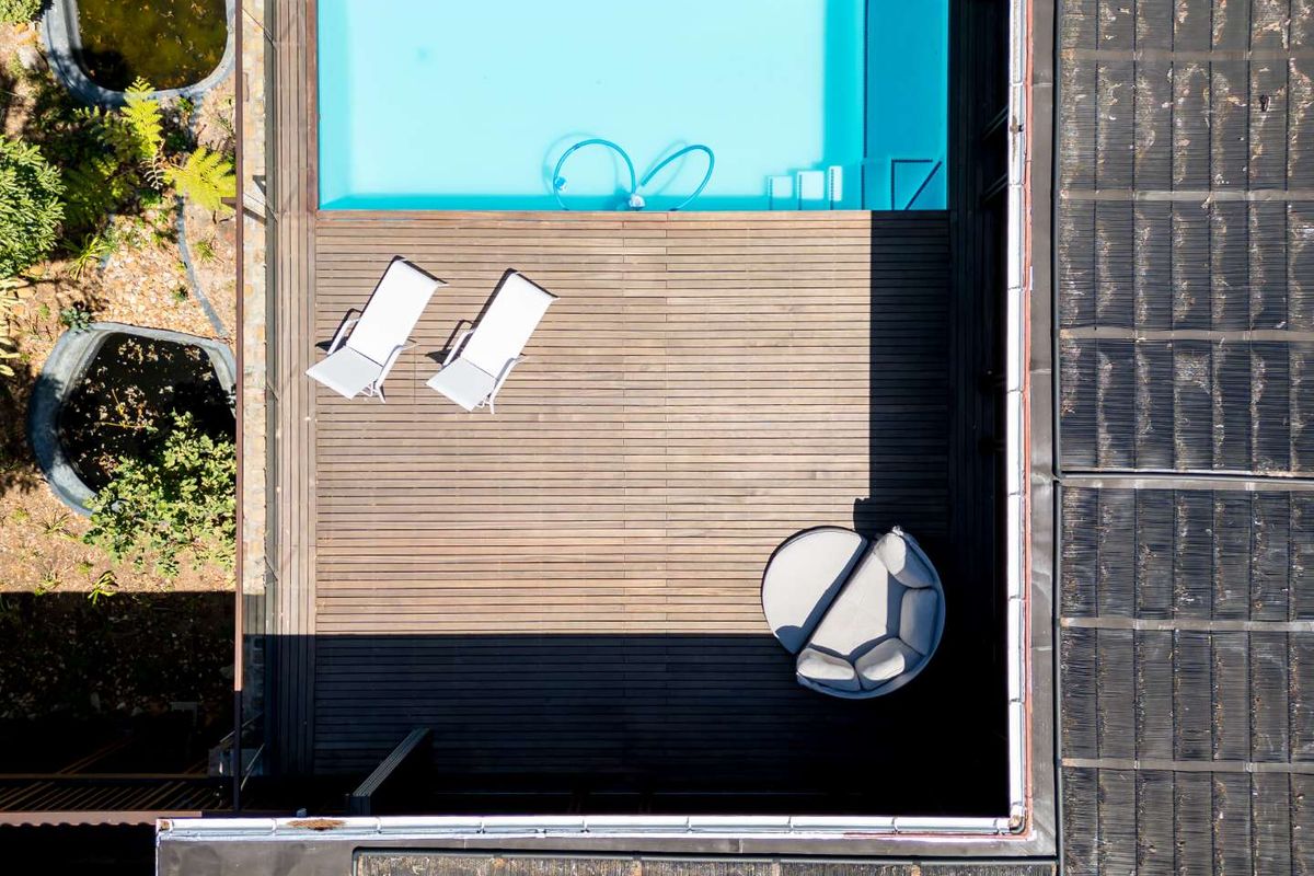 Aerial view of a modern swimming pool area featuring a timber deck, integrated pool, and adjacent landscaped garden space.