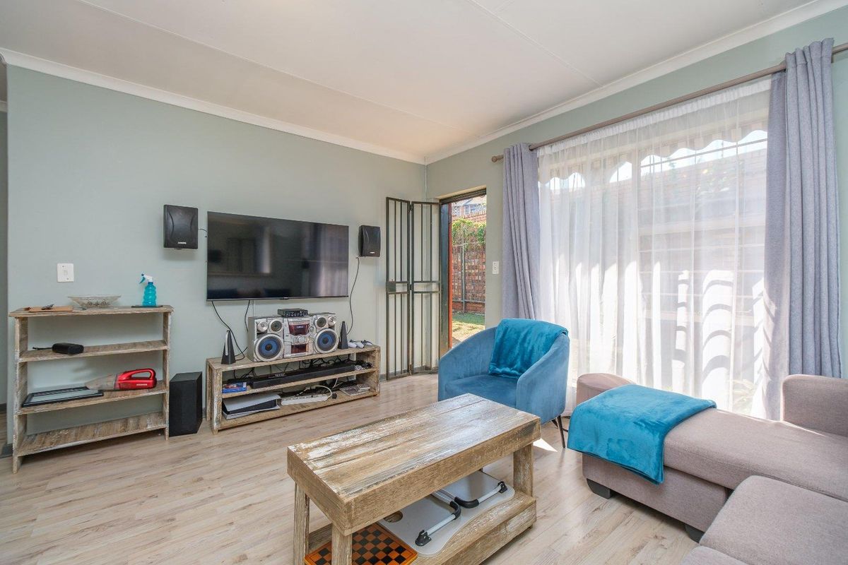 A living room featuring light wood-look laminate flooring, coved ceilings, and a security gate leading to the exterior.