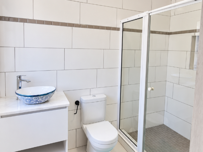 A modern bathroom featuring a vessel sink on a white vanity, a toilet, and a glass-enclosed shower with neutral wall and floor tiling.