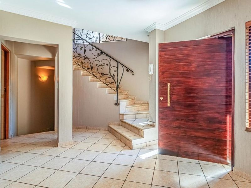 Spacious entrance hall featuring tiled flooring, a solid wood pivot door, and an elegant staircase with decorative wrought iron railing.