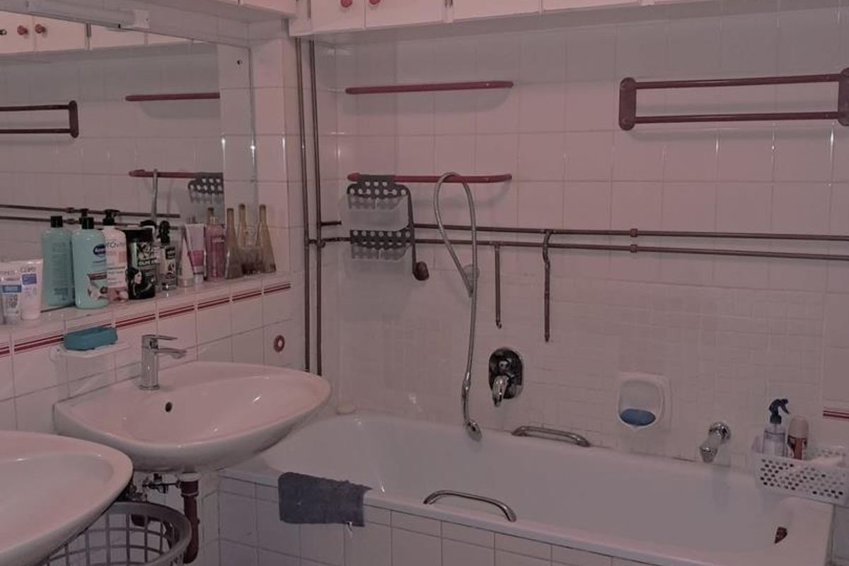 A dated bathroom featuring a bathtub with shower attachment, dual vanity sinks, and extensive wall-mounted storage cabinetry with tiled finishes.