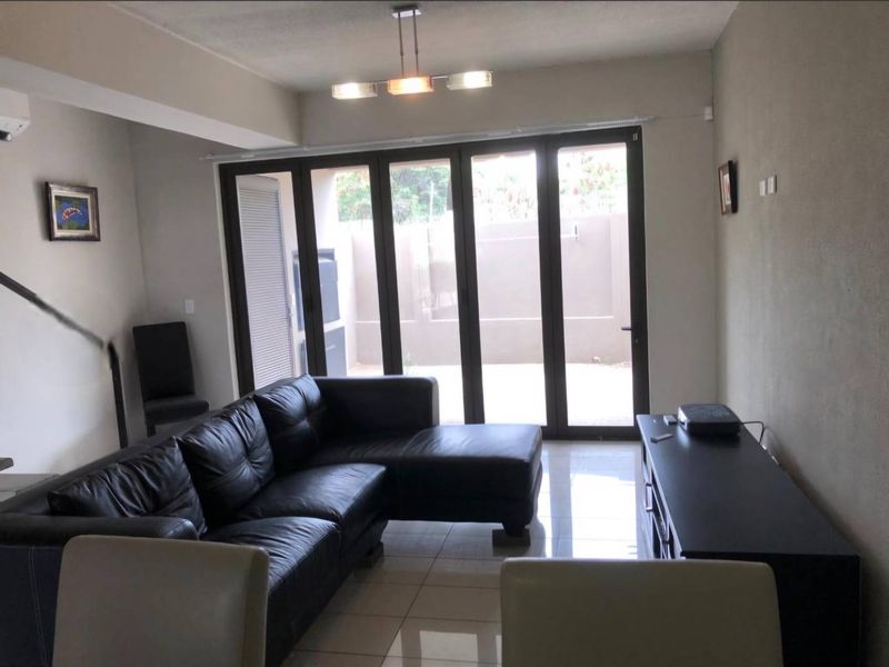 A living room featuring tiled flooring, a ceiling light fixture, and large bi-fold glass doors providing access to the outdoor area.