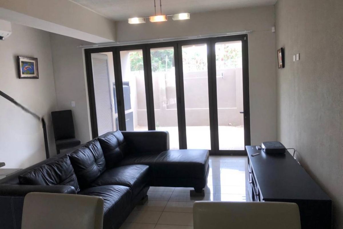 A living room featuring tiled flooring, a ceiling light fixture, and large bi-fold glass doors providing access to the outdoor area.