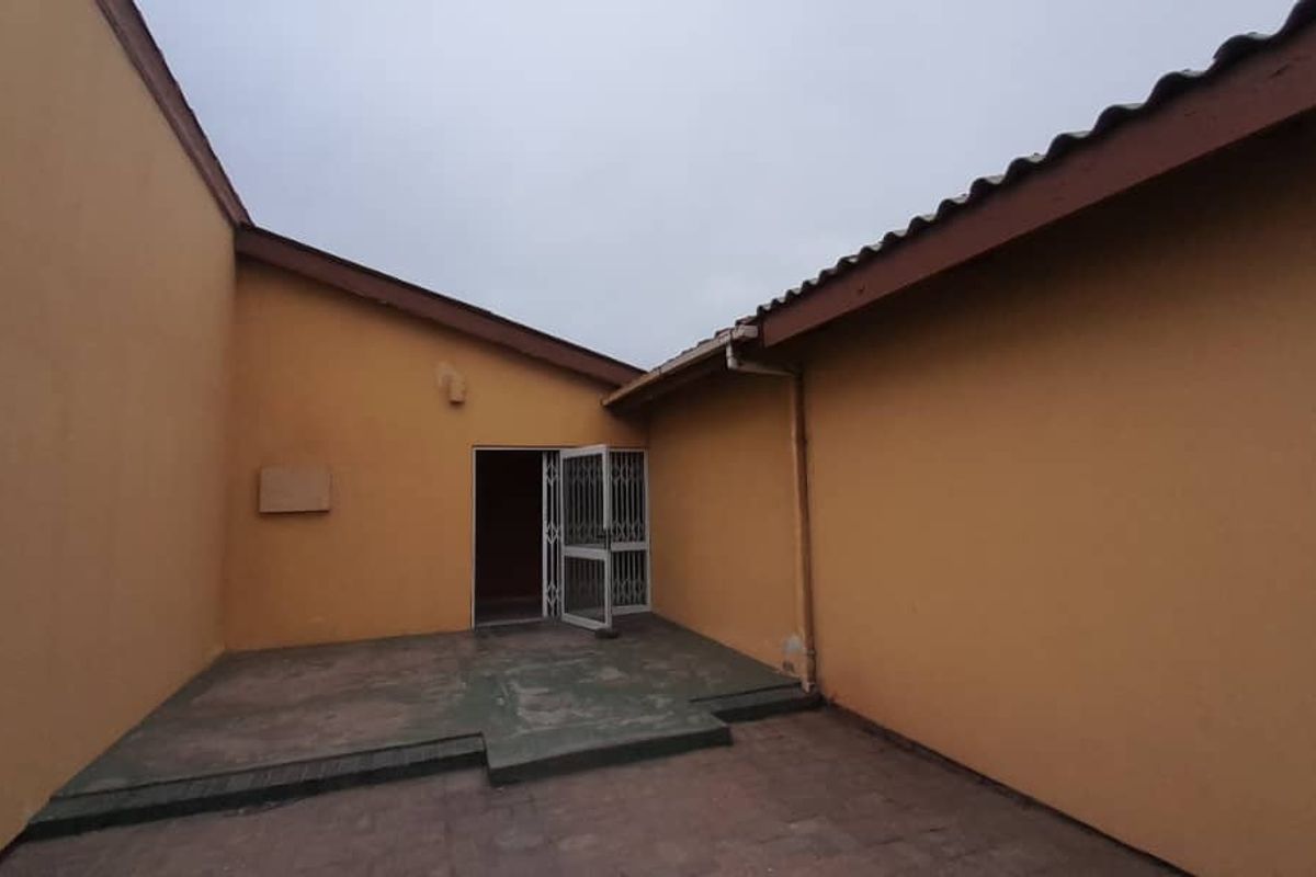 A rear exterior view of the property featuring a paved patio area, security gate, and plain exterior walls.