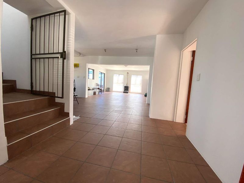 Spacious open-plan living area featuring tiled flooring, a built-in staircase with a security gate, and a freestanding fireplace in the rear section.