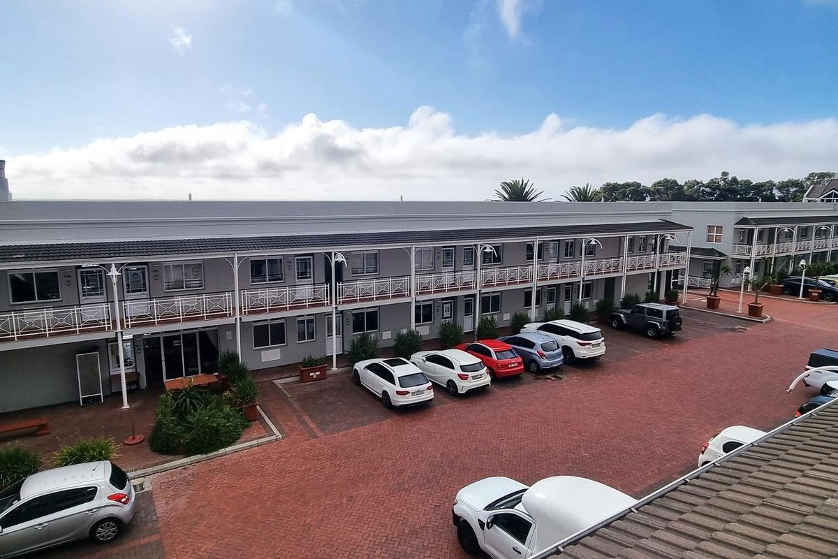 An elevated view of a commercial office complex featuring a paved courtyard, parking area, and multi-level building with external walkways and balconies.