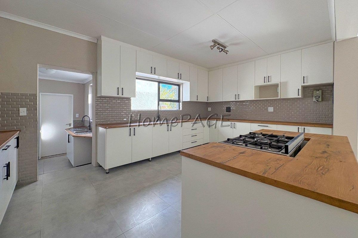Modern kitchen featuring white cabinetry, timber-look countertops, gas hob, and subway tile backsplash, with an adjoining scullery area.
