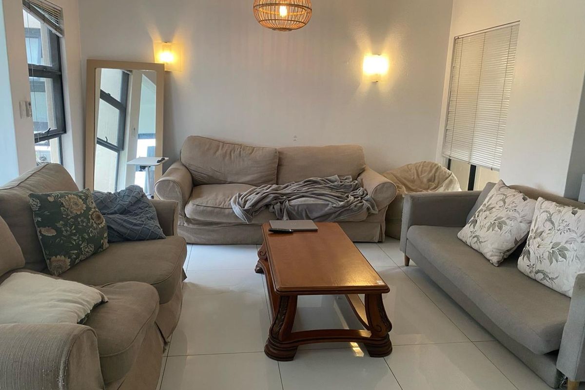 A bright living room featuring large format floor tiles, wall-mounted lighting, and windows fitted with venetian blinds.