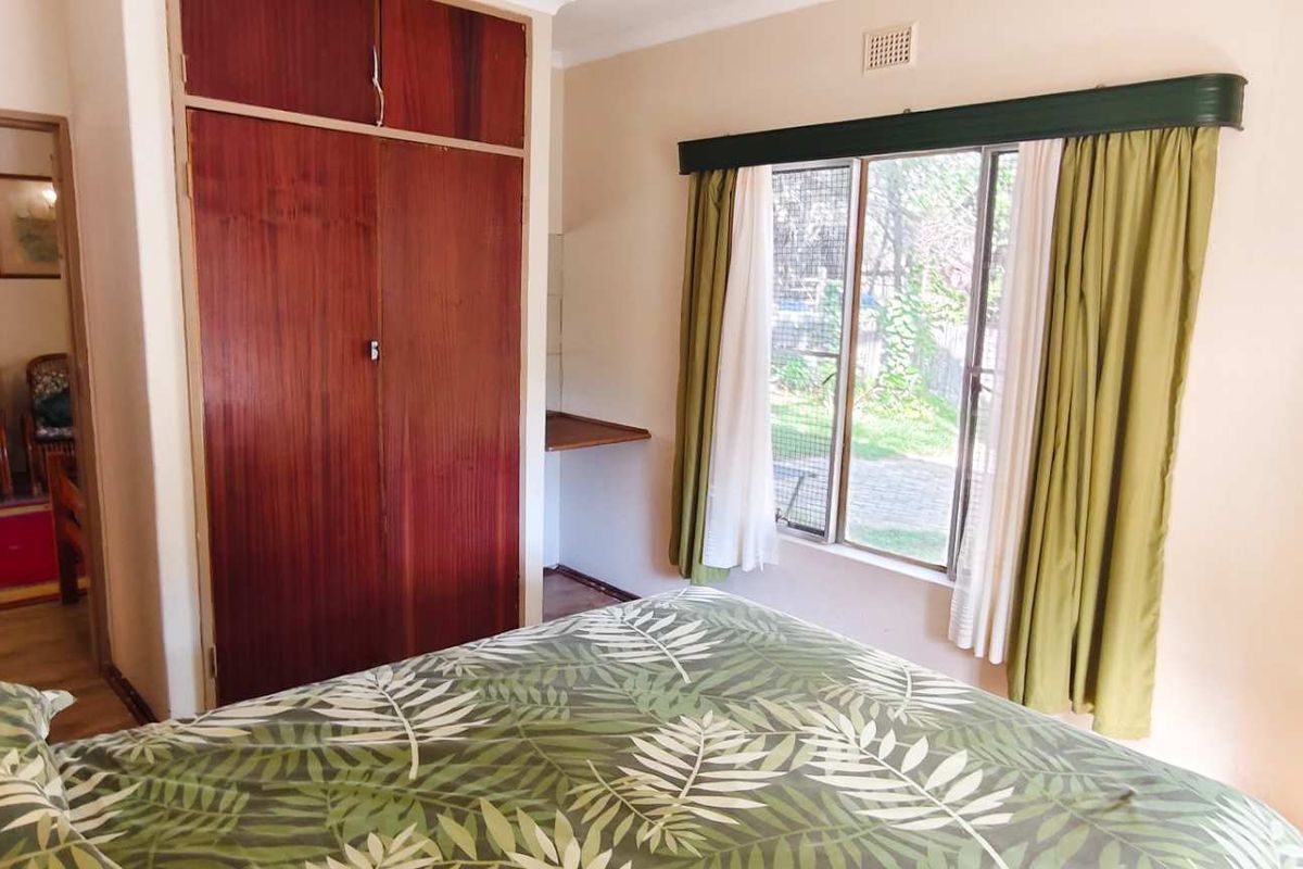 A bedroom featuring built-in wooden cupboards, a window with garden views, and neutral wall finishes.
