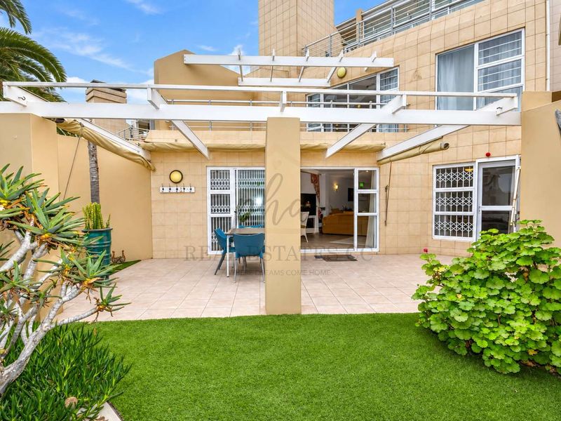 A well-maintained rear patio area featuring a pergola, tiled flooring, and artificial lawn, providing seamless indoor-outdoor flow through sliding glass doors.