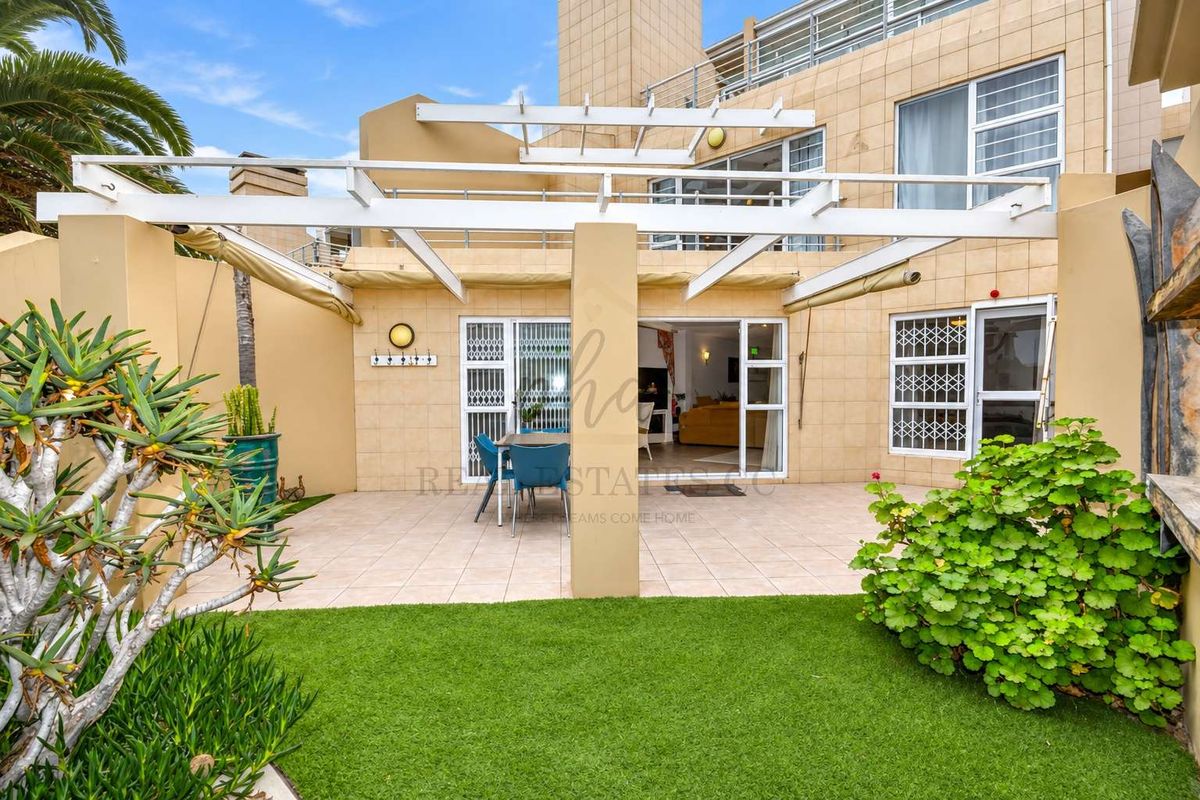 A well-maintained rear patio area featuring a pergola, tiled flooring, and artificial lawn, providing seamless indoor-outdoor flow through sliding glass doors.