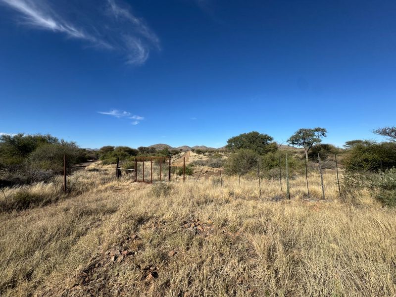 Expansive open veld area featuring natural vegetation, wire perimeter fencing, and a metal access gate under a clear blue sky.