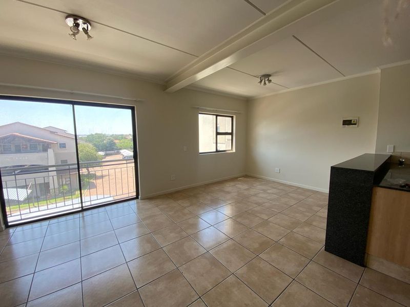 Spacious open-plan living area featuring tiled flooring, a granite kitchen counter, and a sliding glass door leading to a balcony.