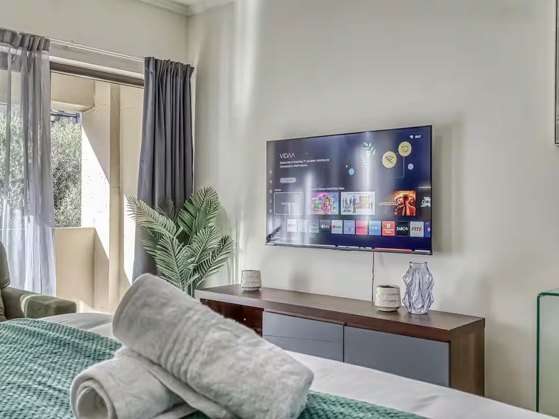A well-lit bedroom featuring a wall-mounted television and a sliding glass door providing access to an outdoor balcony area.