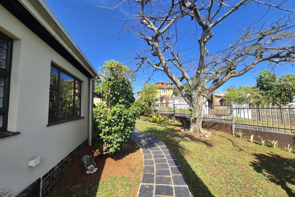 A view of the rear garden featuring a paved walkway, established tree, and secure metal perimeter fencing along the boundary wall.