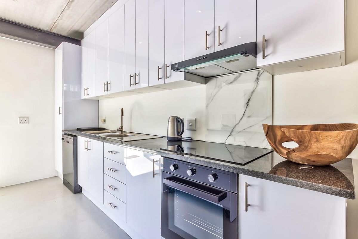 Modern kitchen featuring high-gloss white cabinetry, dark granite countertops, a built-in oven, glass hob, extractor fan, and a marble-look splashback.