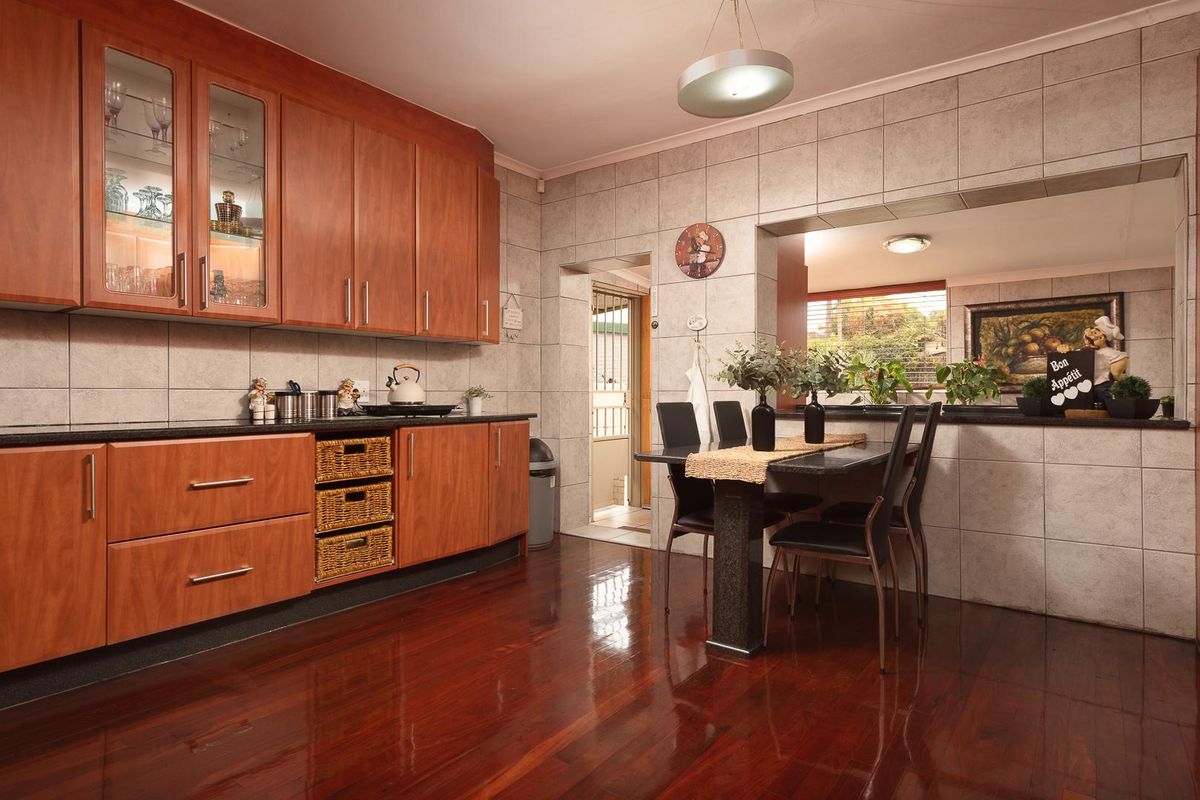 A functional kitchen featuring warm-toned wooden cabinetry, dark granite countertops, and polished hardwood flooring, with a convenient pass-through window to the adjacent dining area.