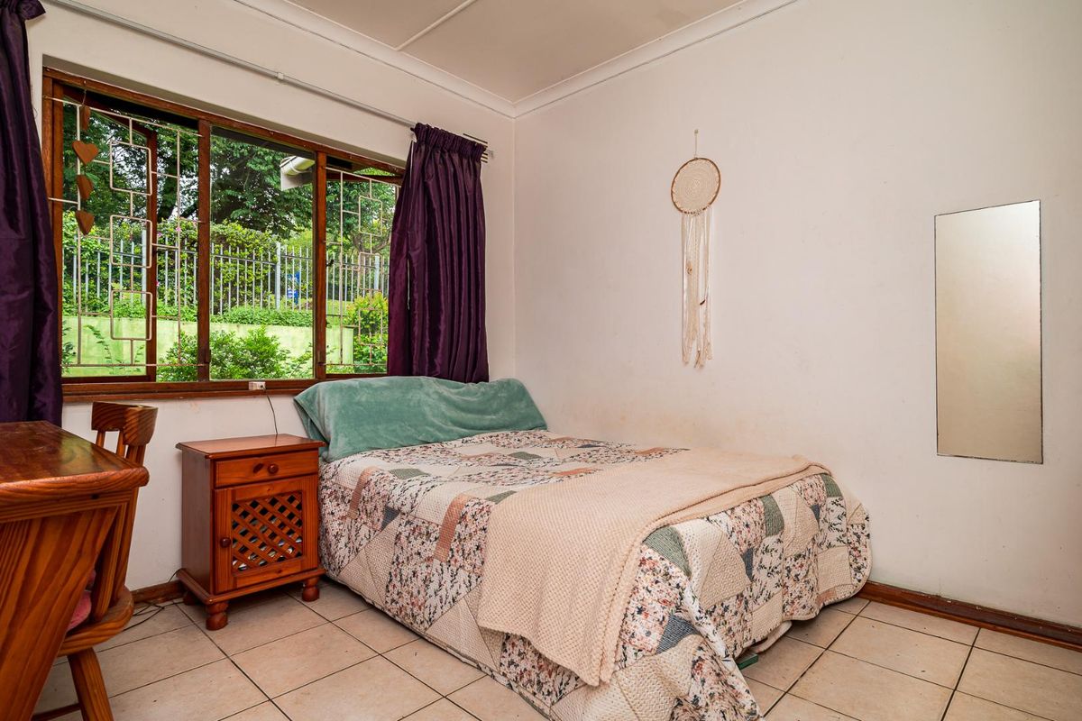 A bedroom featuring tiled flooring, a large window with security bars, and neutral wall finishes.