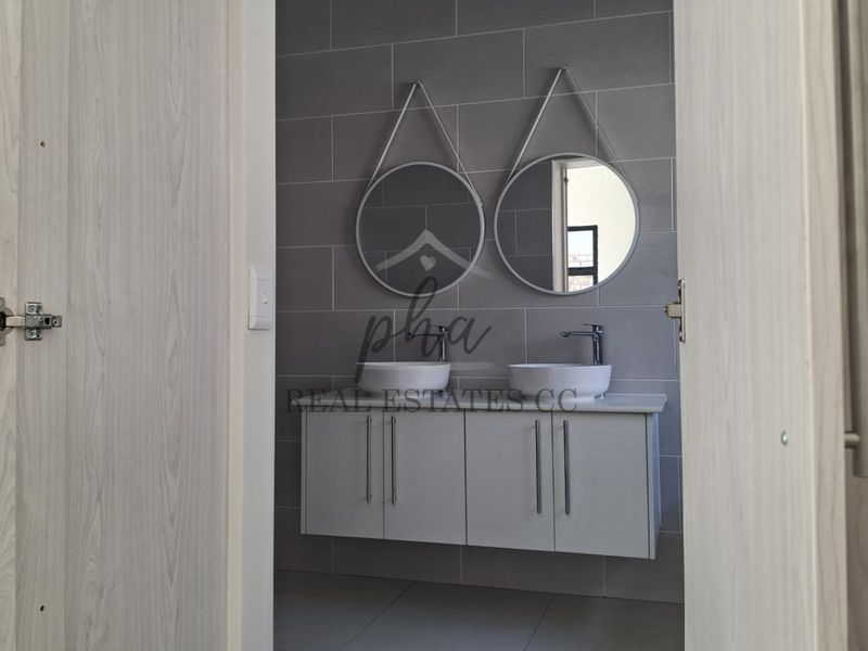 Modern bathroom featuring a double vanity with vessel sinks, wall-mounted cabinetry, and contemporary grey wall tiling.