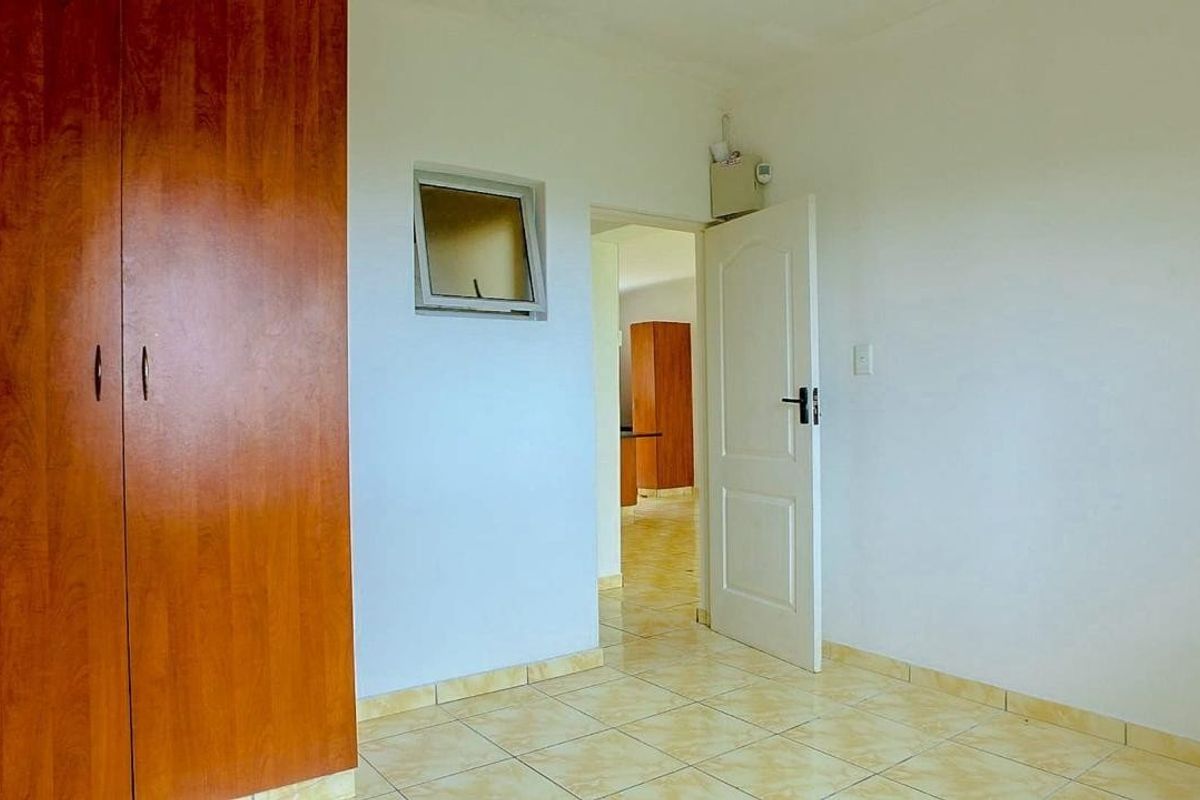 A vacant bedroom featuring built-in wooden wardrobes, tiled flooring, and a top-hung window, with a doorway leading to an adjacent room.