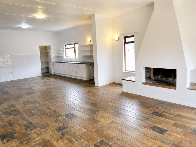 Spacious open-plan living and kitchen area featuring a prominent built-in fireplace, tiled flooring, and functional kitchen cabinetry with a pantry.