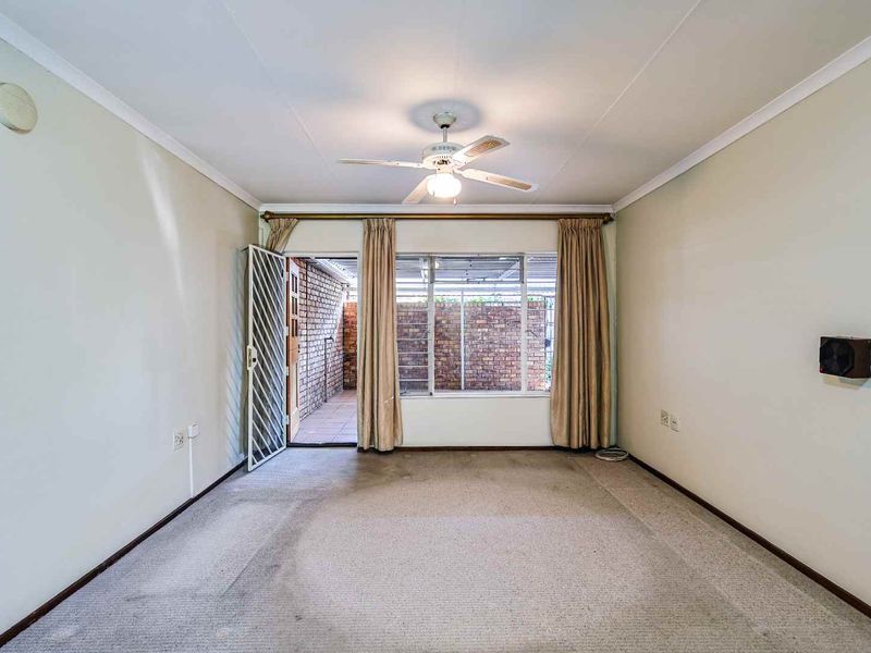 A spacious living room featuring a ceiling fan, neutral walls, and direct access to a private paved patio area.