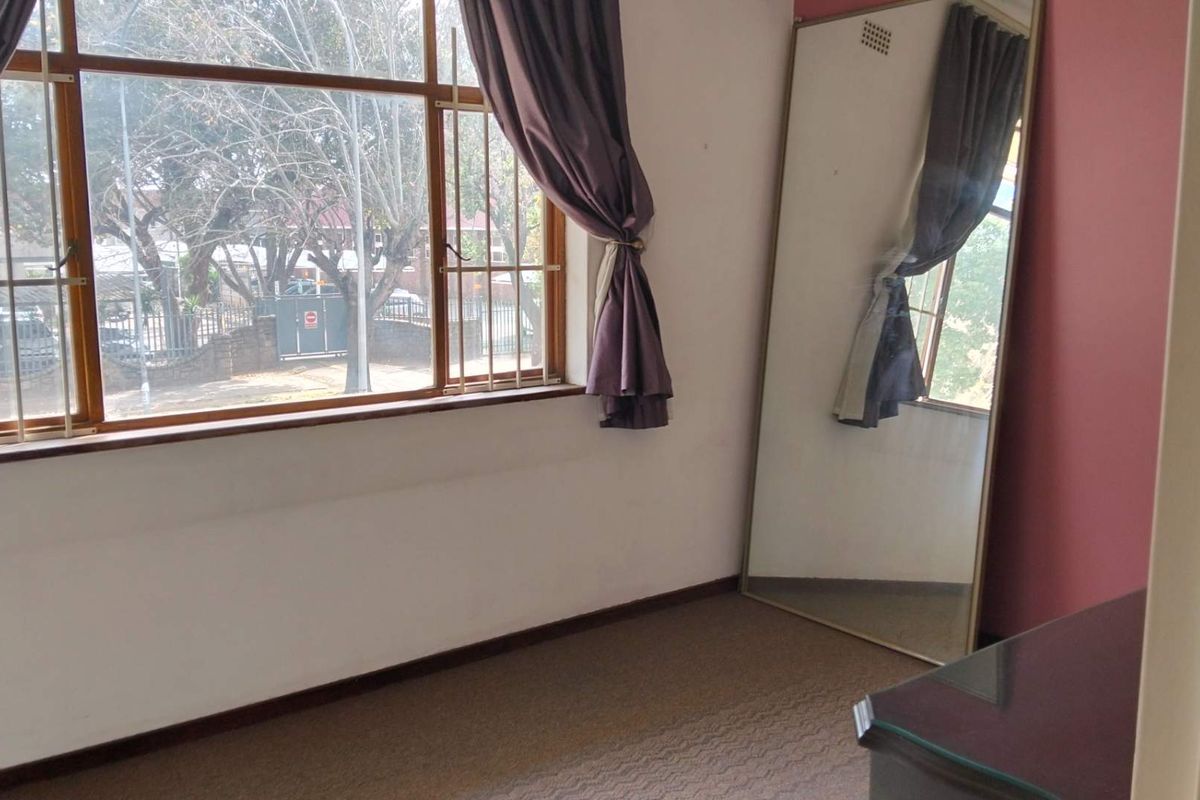 A bedroom featuring large windows with security bars, carpeted flooring, and an accent wall.
