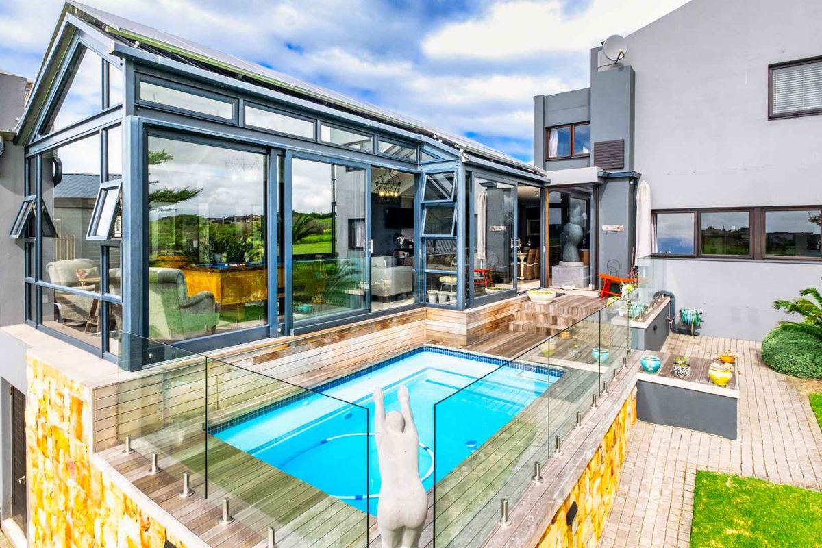 Rear exterior view featuring a modern sunroom, timber decking, and a swimming pool with glass balustrades, set against a contemporary multi-level home.