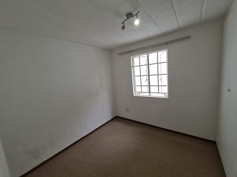 An empty bedroom featuring a grid-pattern window, carpeted flooring, and a textured ceiling, offering a blank canvas for potential updates.